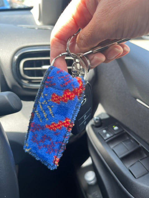 Blue Metroline bus moquette keyring with red and orange pattern, held alongside car keys