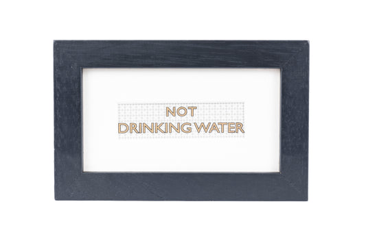 A black frame with a white background and a Not drinking water gold text on a small Formica print background