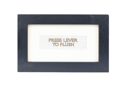 A black frame with a white background and a Press lever to flush gold text on a small Formica print background