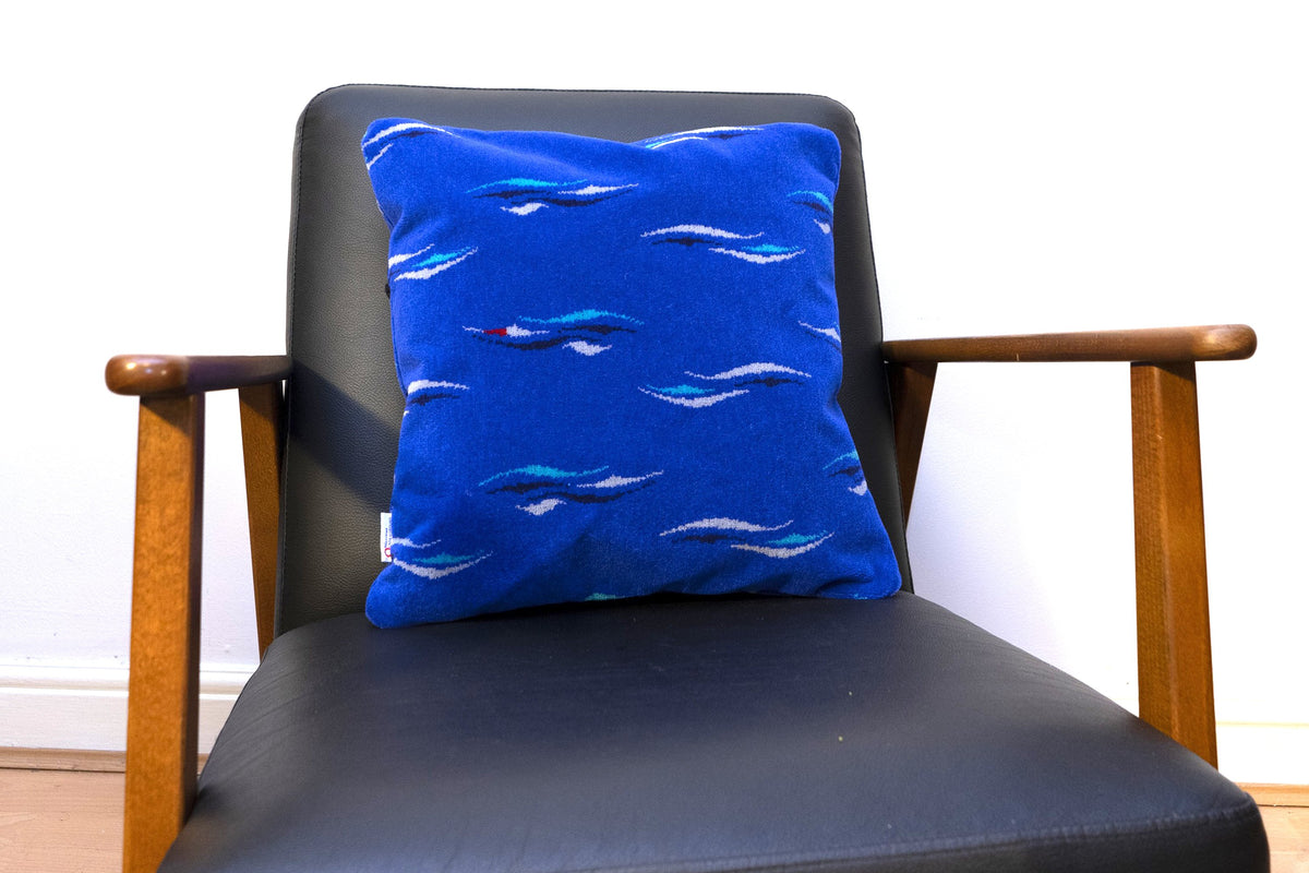 Blue DLR moquette cushion on an armchair, featuring scattered turquoise, pale grey and dark wave motifs with small red accents.